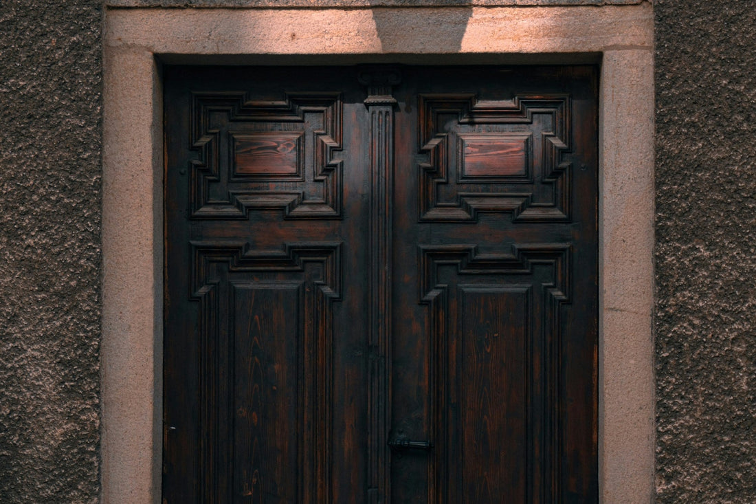 A heavy dark wooden double door, closed, set in a pale stone doorway