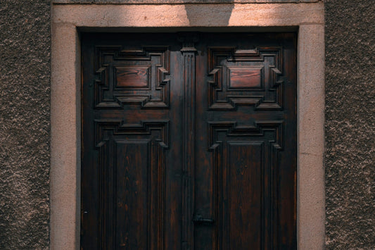 A heavy dark wooden double door, closed, set in a pale stone doorway