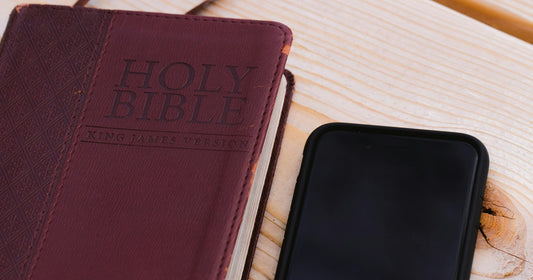 A burgundy leather Holy Bible lying beside a switched-off mobile phone on a pale wooden table